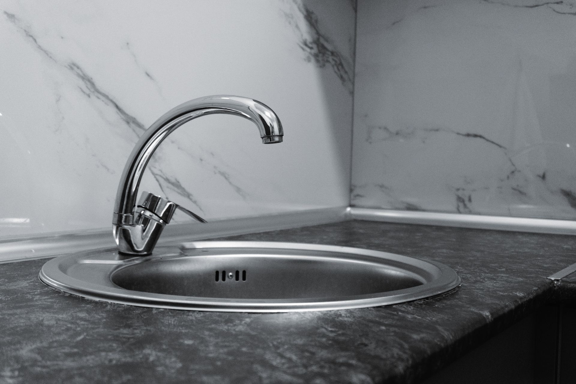 Stainless steel kitchen sink and faucet against marble backsplash in a modern kitchen.